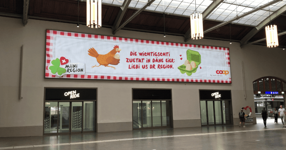 Halle im Bahnhof Basel SBB mit grossem Banner der Werbung.